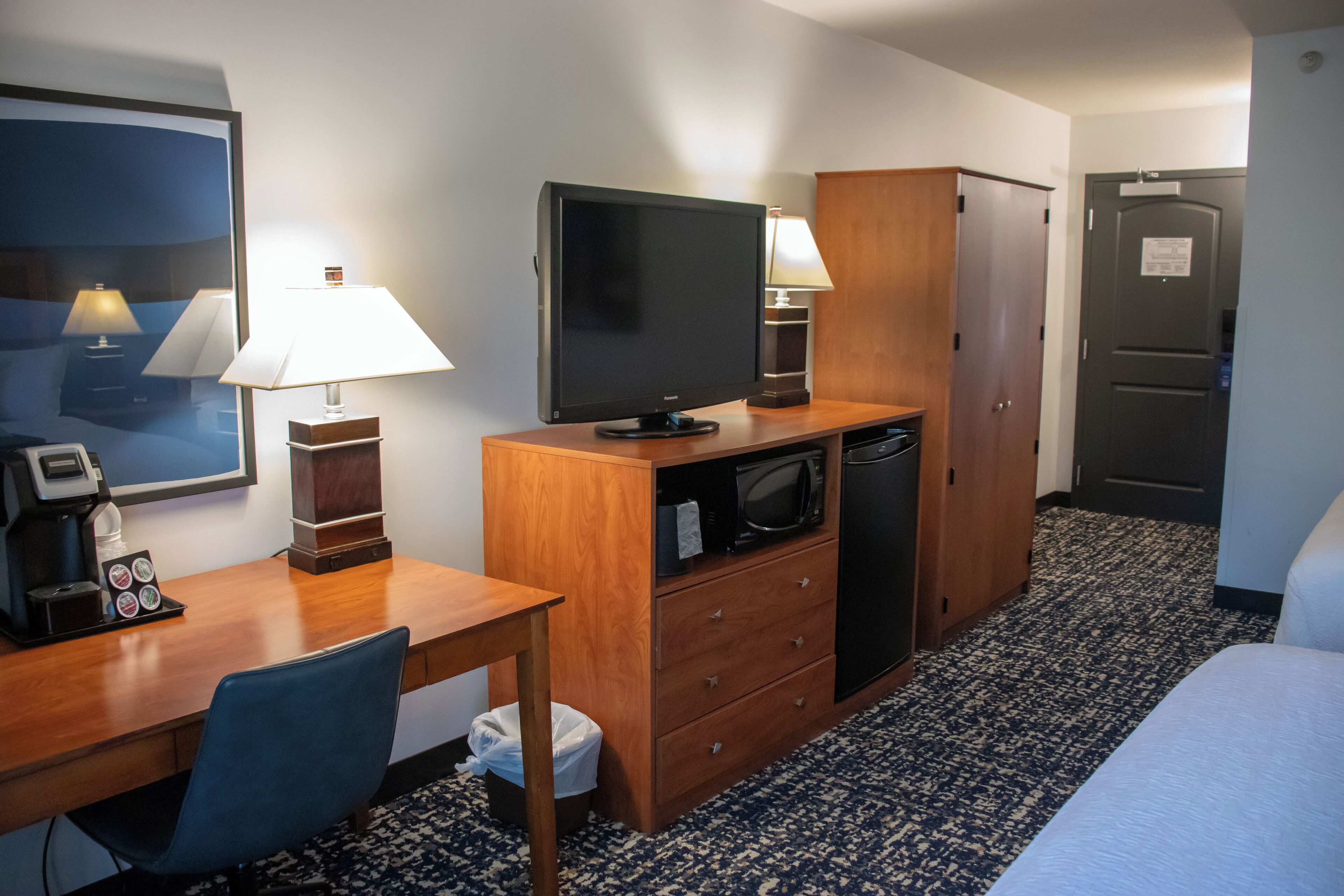 Een hotelkamer met een houten bureau, een televisie, een magnetron, een koelkast, een bed en een deur.