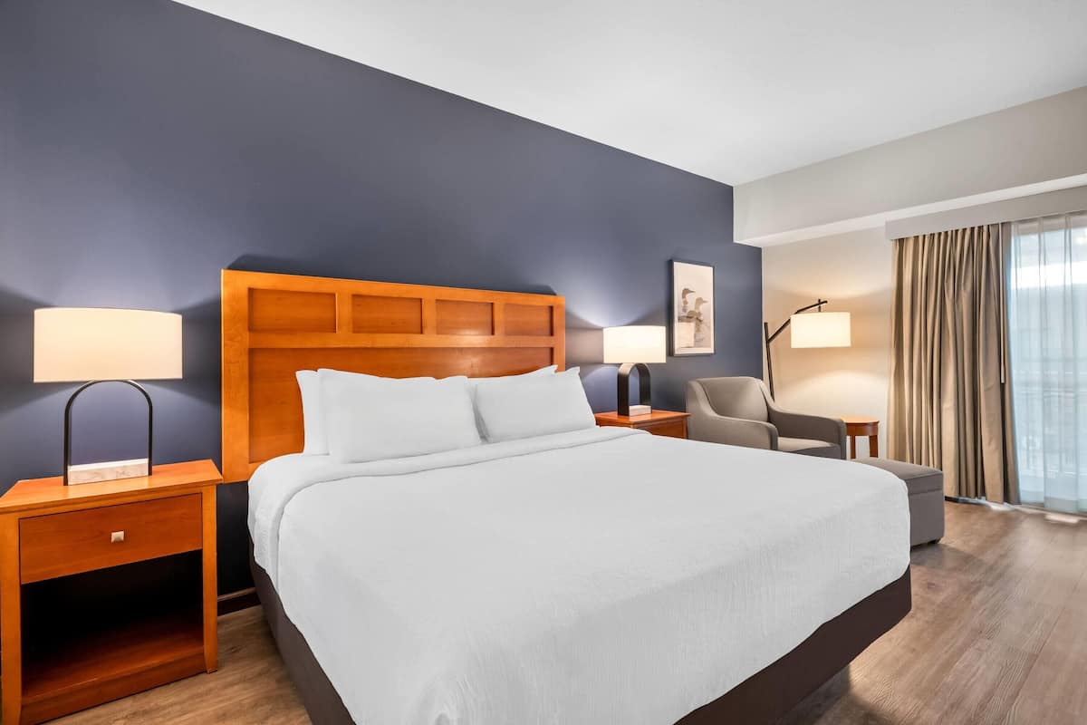 A hotel room with a large bed, two bedside tables, a chair, a desk, and a window with curtains.