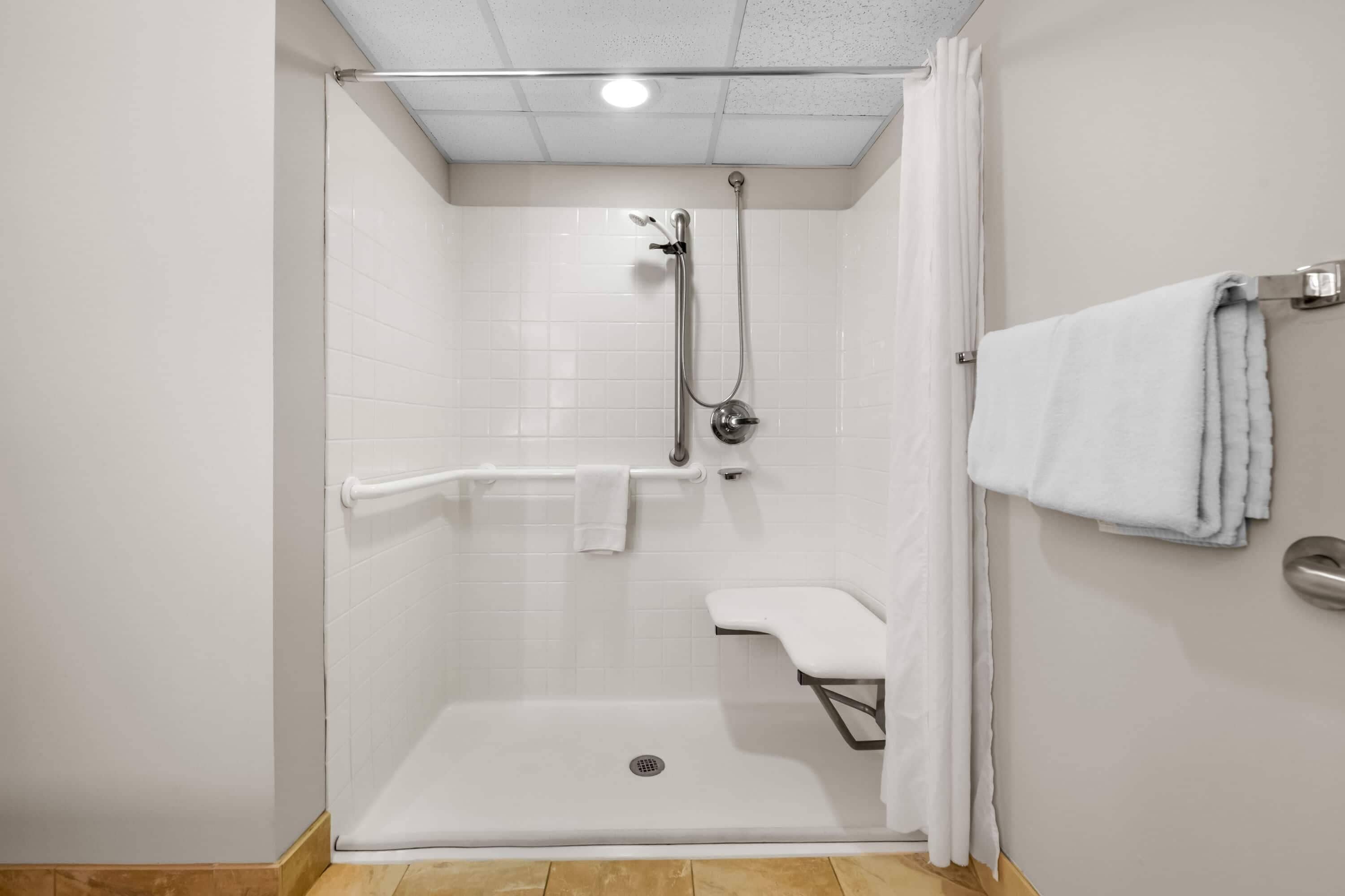 A shower with a handheld showerhead, a handheld showerhead, a grab bar, and a towel rack.