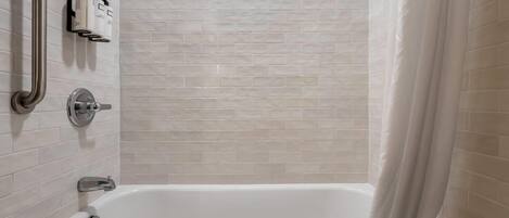 A bathroom with a bathtub, a shower area, and a handrail.