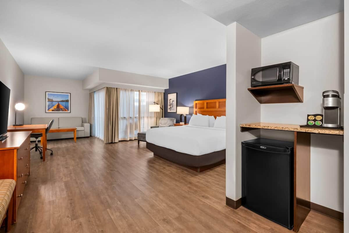 A hotel room with a bed, desk, chair, and a small refrigerator.