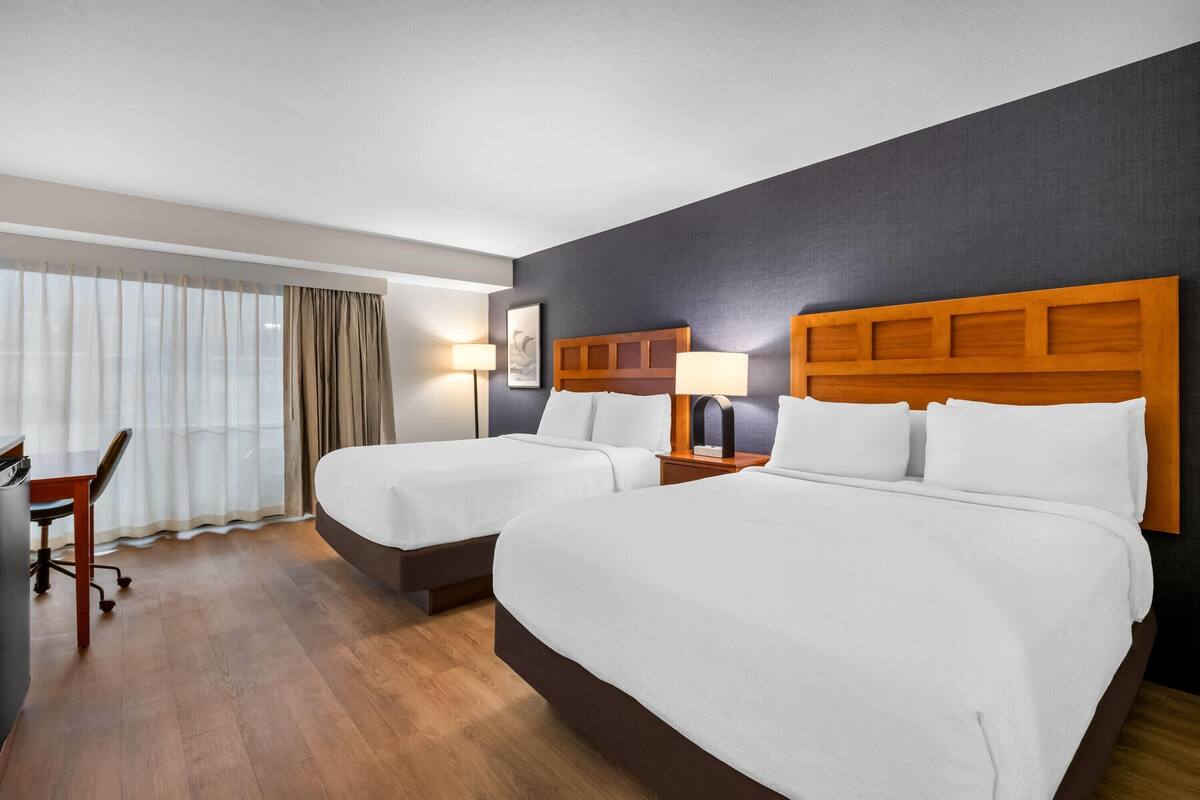 A hotel room with two beds, a desk, and a chair.