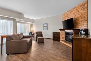 Een moderne woonkamer met een bank, voetenbankje, flatscreen televisie, open haard en houten vloeren.