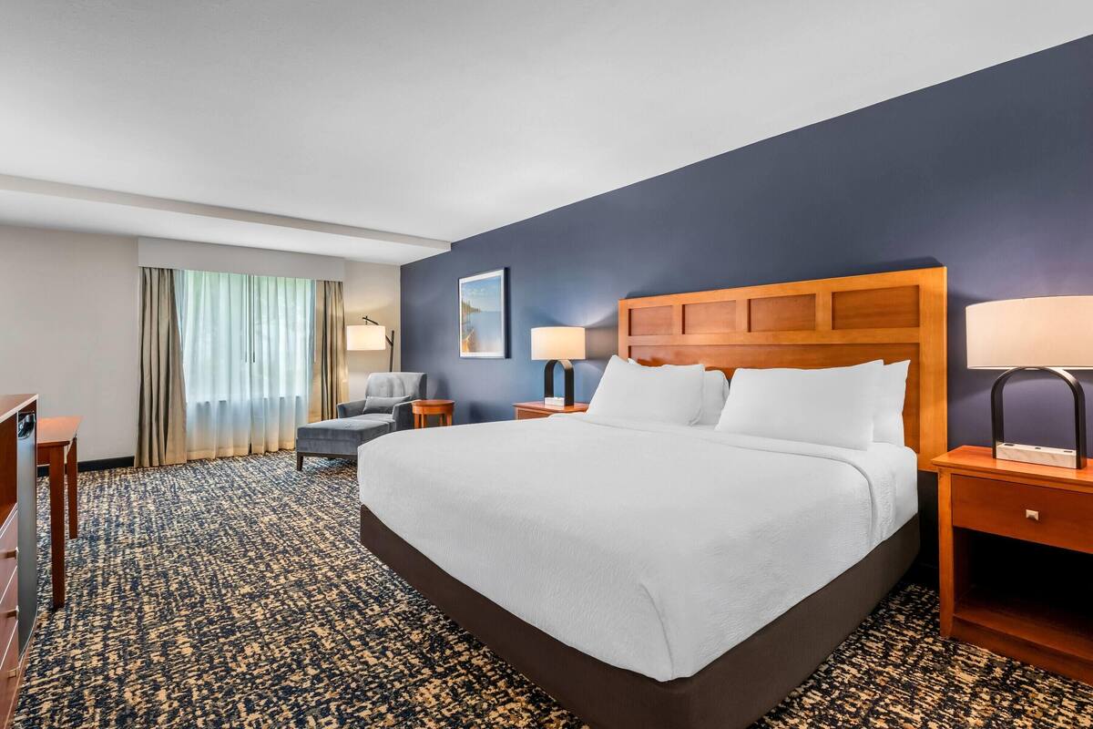 A hotel room with a large bed, two bedside tables, a desk, a chair, and a window with curtains.