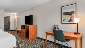 A hotel room with a bed, a desk with a chair, a television on a wooden cabinet, a framed picture on the wall, and a lamp.