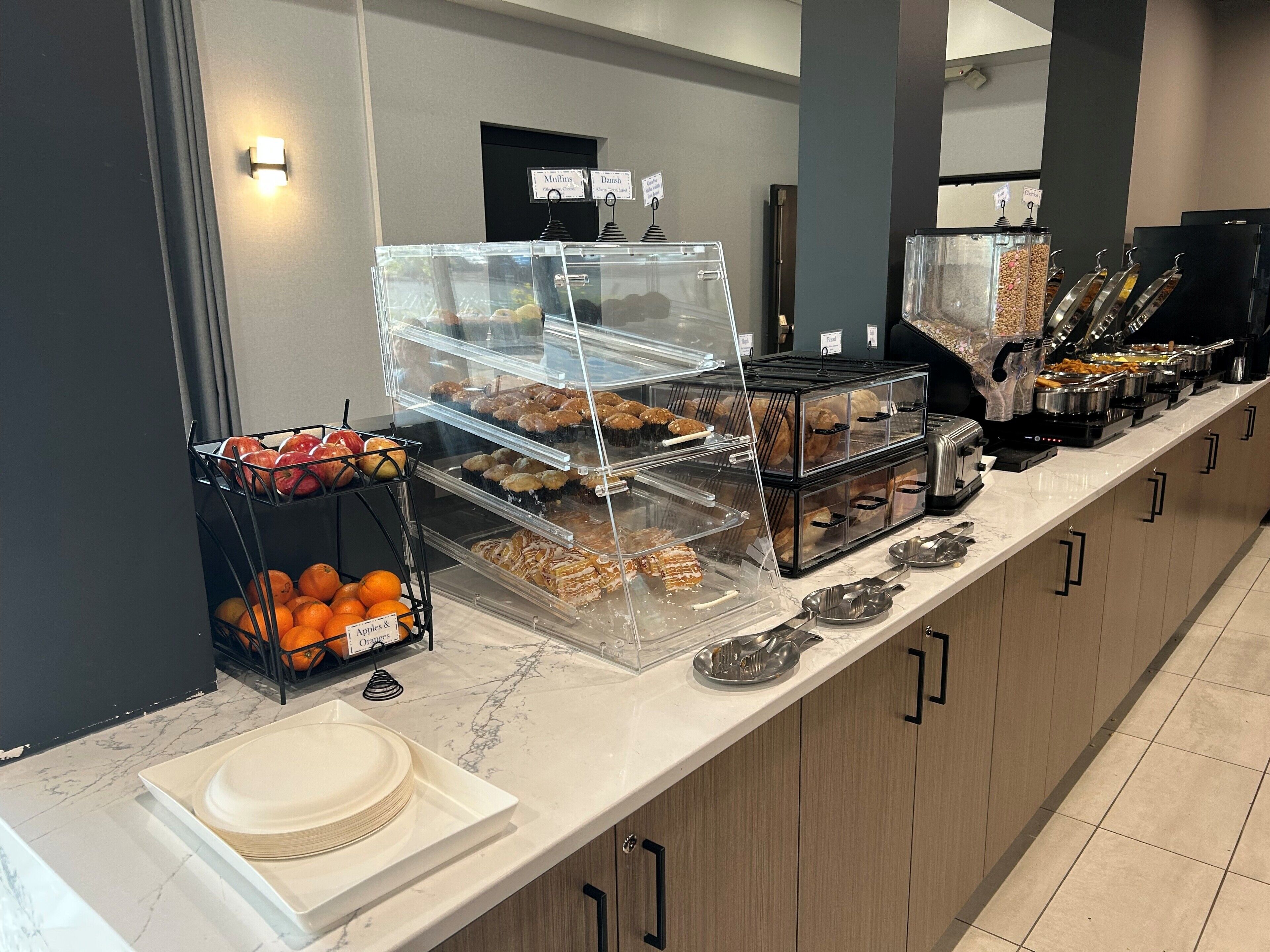 A buffet counter with various food items and a sign indicating the availability of muffins and Danish.
