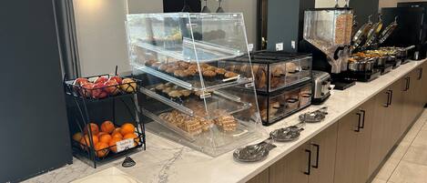 Un mostrador de buffet con diversos alimentos y un cartel que indica la disponibilidad de muffins y danesas.