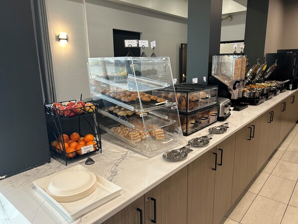 Un mostrador de buffet con diversos alimentos y un cartel que indica la disponibilidad de muffins y danesas.