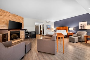 Een moderne hotelkamer met een flatscreen televisie, een open haard, een bank, een bed en een eettafel.