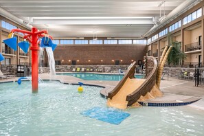 An indoor swimming pool with a slide, a water feature, and a brick wall.