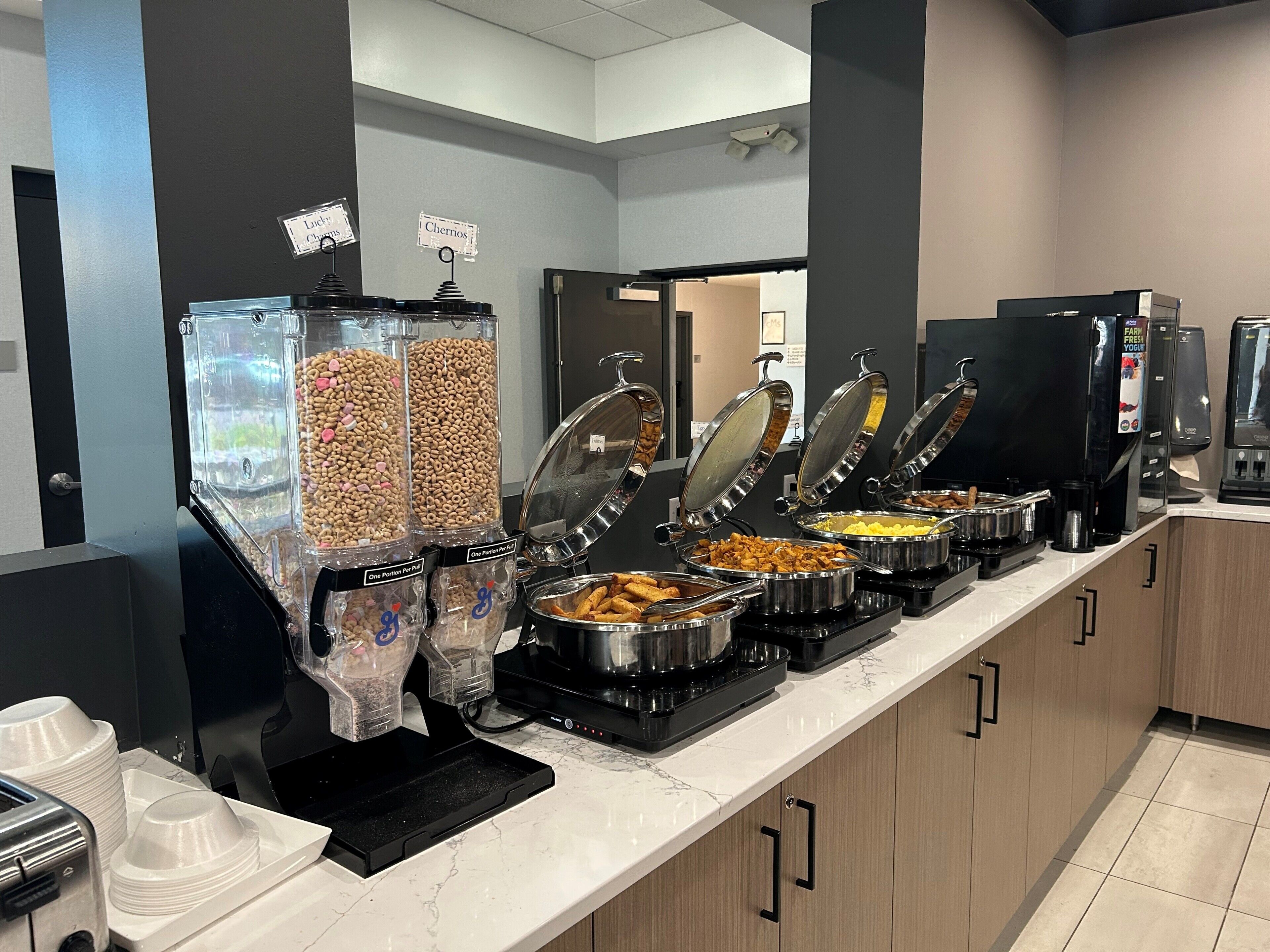 Zona de buffet con diferentes dispensadores de alimentos y una máquina de café.