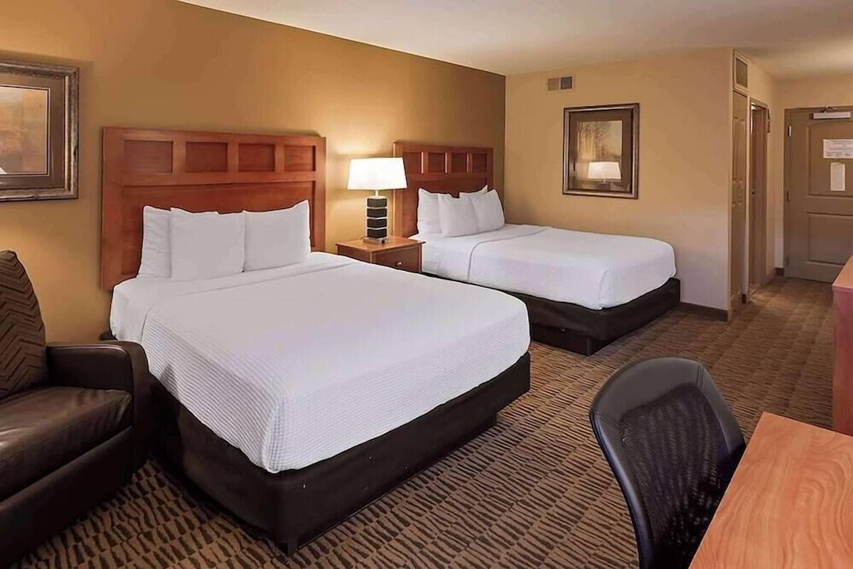 A hotel room with two beds, a desk, a chair, and a couch.