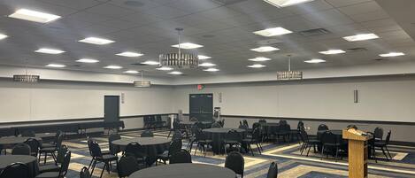 A conference room with multiple tables and chairs, a podium, and a carpeted floor.