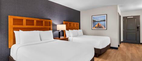 A hotel room with two beds, a nightstand with a lamp, a painting on the wall, and a door.