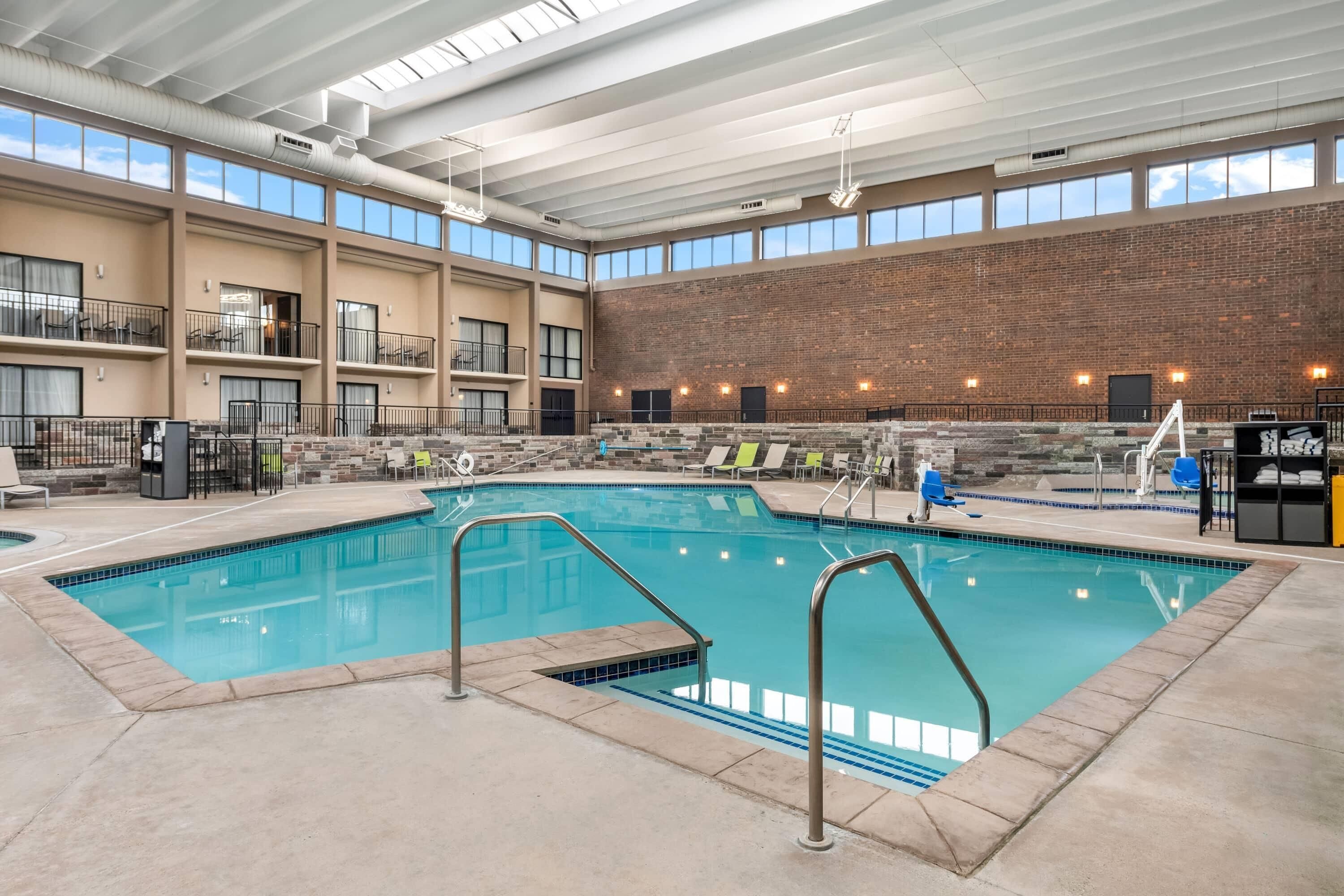 An indoor swimming pool with a high ceiling, large windows, and a brick wall.