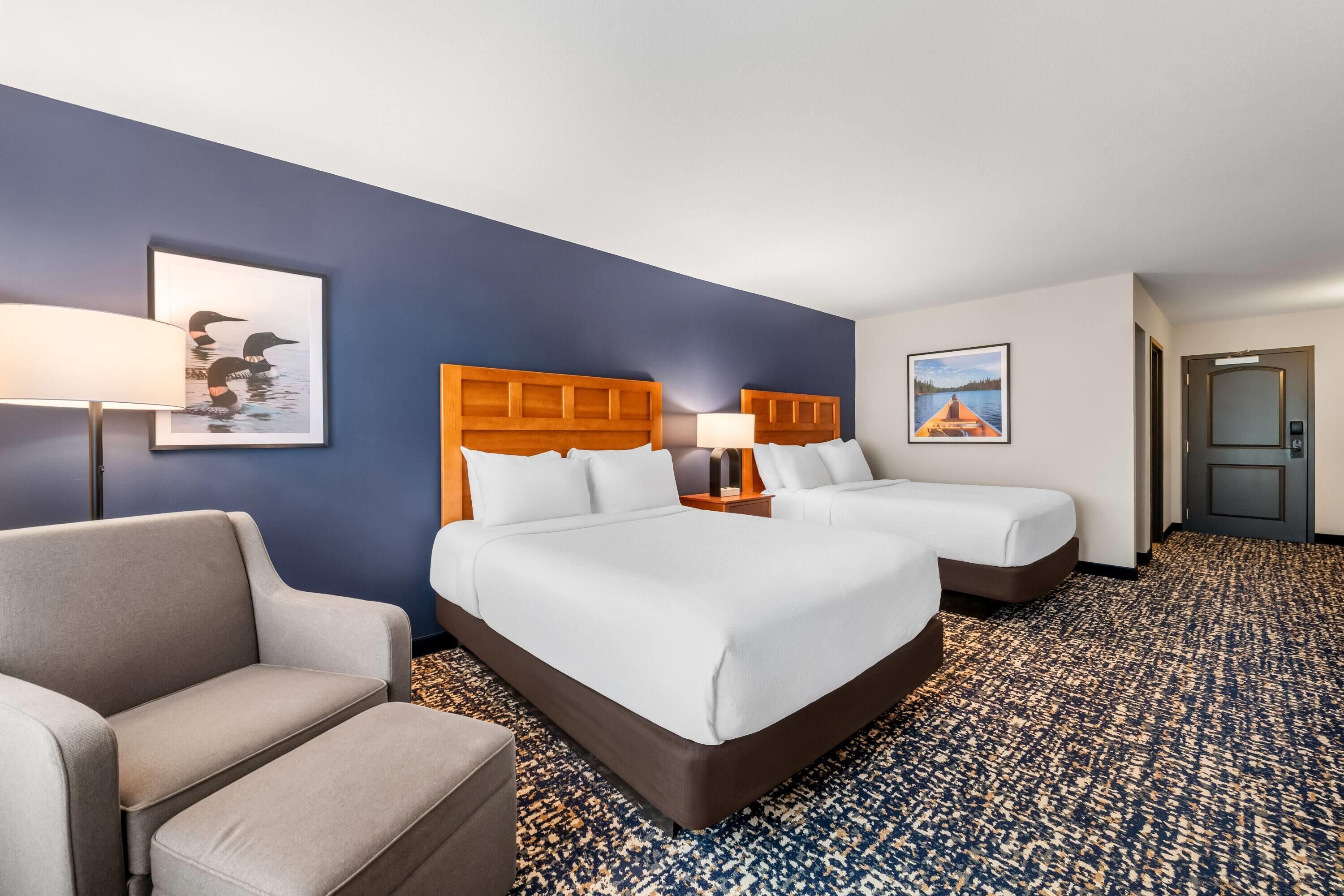 A hotel room with two beds, a sofa, a lamp, and artwork on the walls.