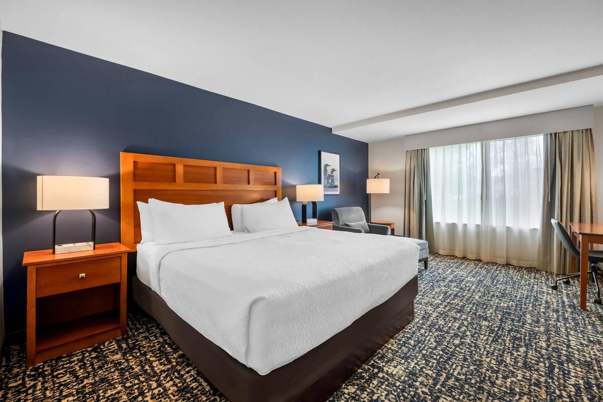 A hotel room with a large bed, two bedside tables with lamps, a desk, and a chair.