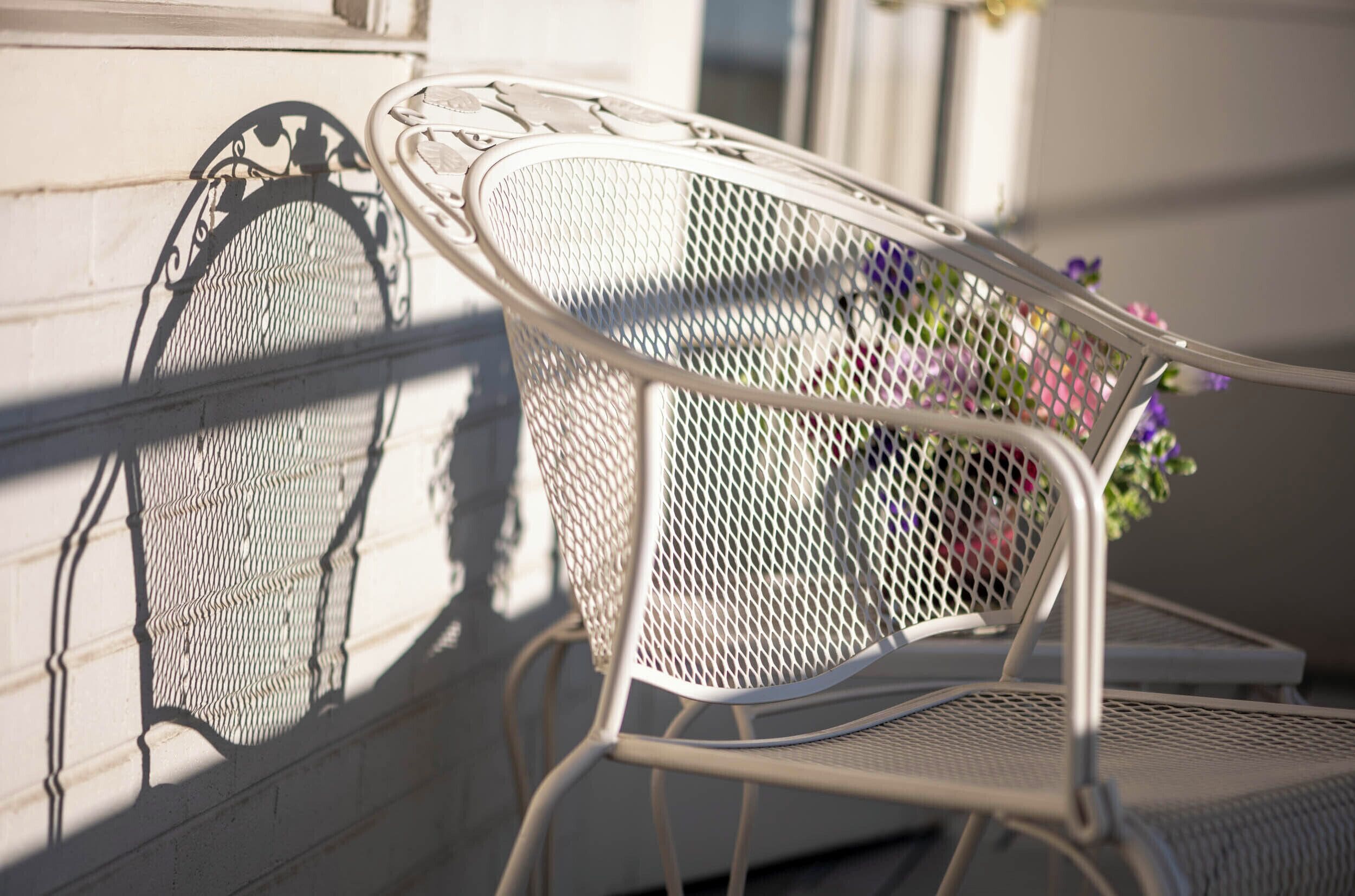 Une chaise en métal dotée d’un dossier et de repose-bras en treillis, placée à côté d’un mur orné d’une rampe décorative en métal.