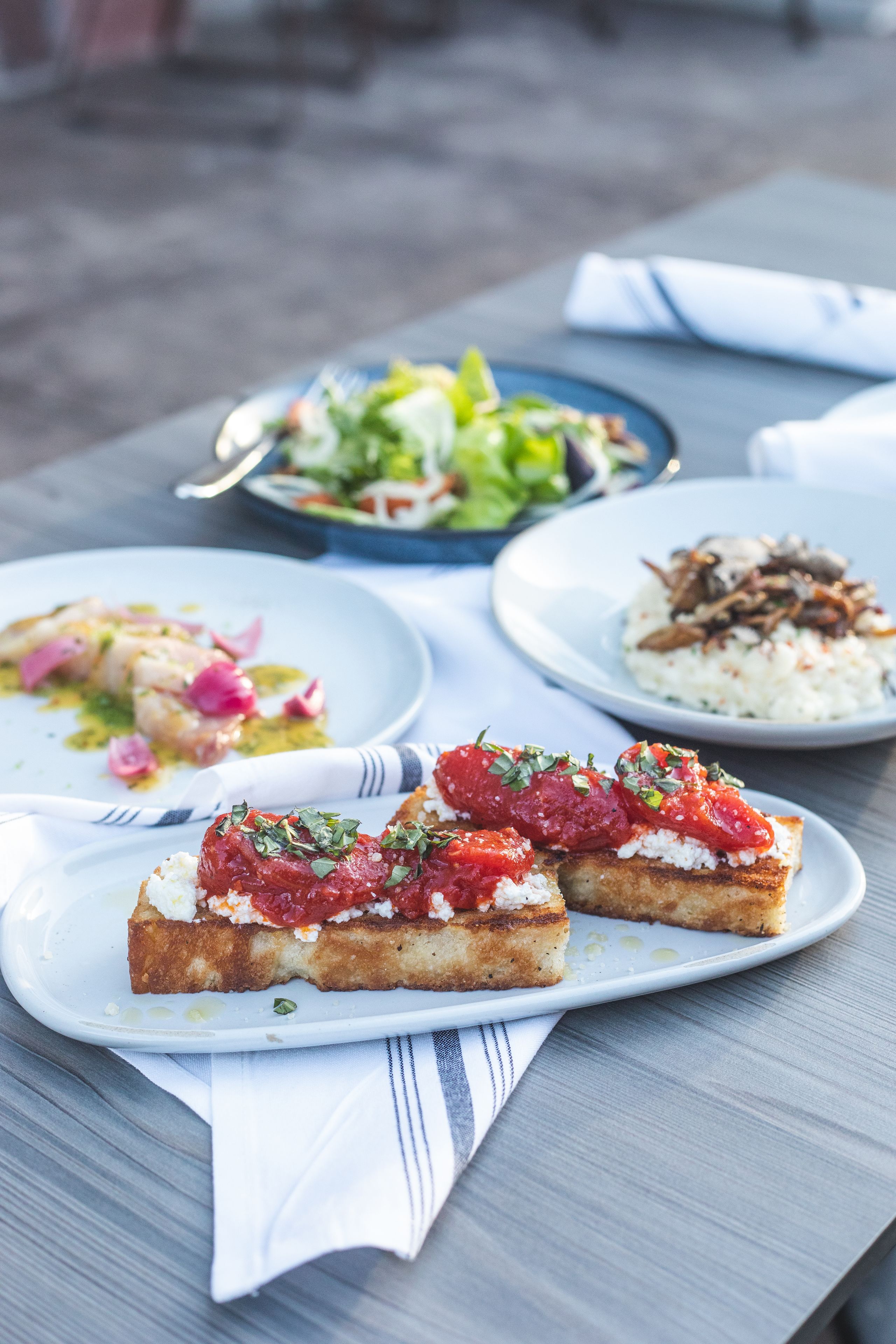 A table with three plates of food, including a salad, rice with mushrooms, and bruschetta.
