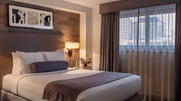 Une chambre d’hôtel avec un grand lit, une table de chevet avec une lampe, une œuvre d’art encadrée au mur et une fenêtre avec des rideaux.