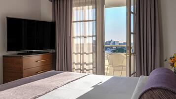 Une chambre d’hôtel avec un lit, un téléviseur posé sur une commode en bois, un balcon avec une chaise et une vue sur la ville.
