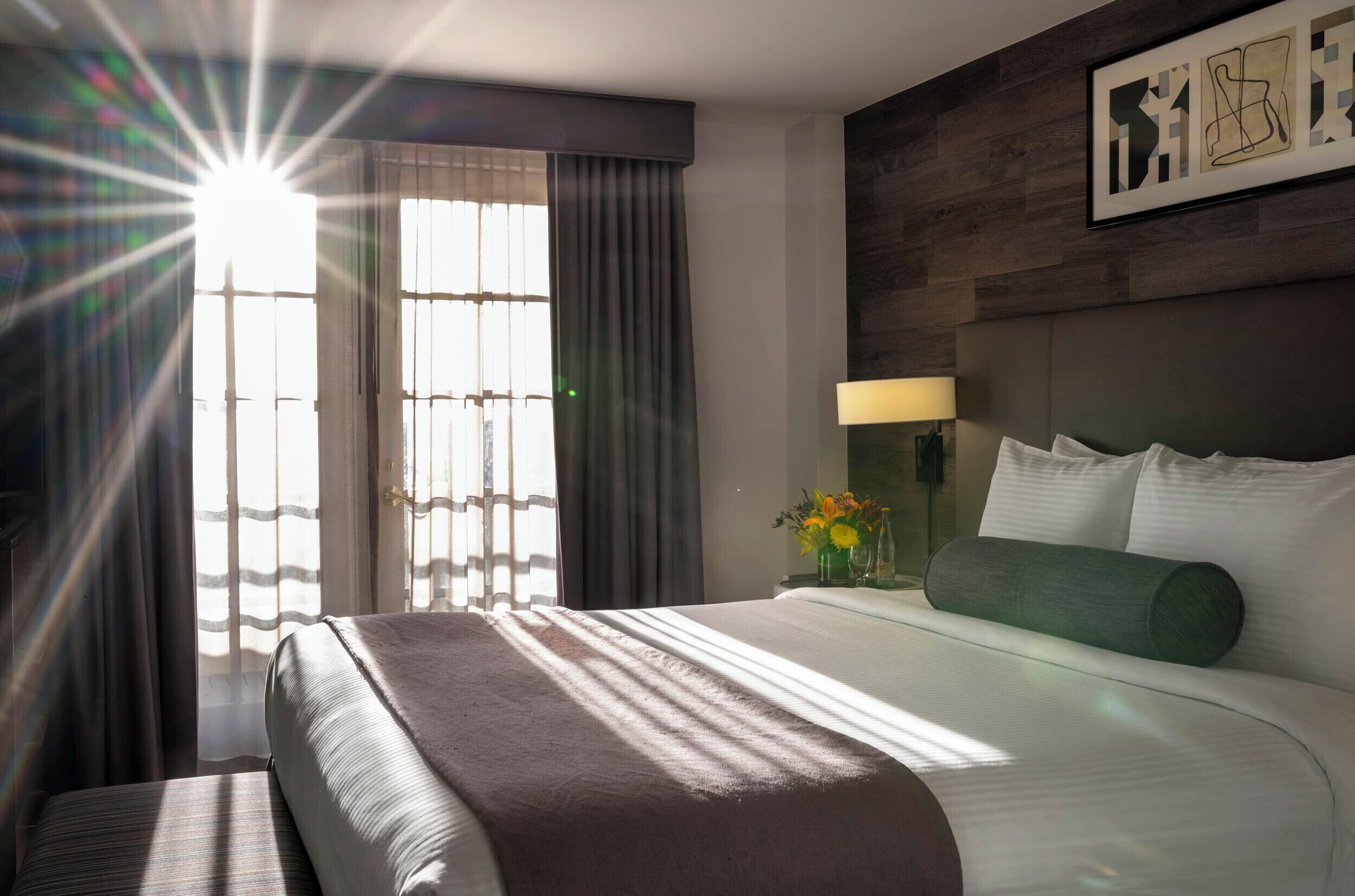 A hotel room with a large bed, a nightstand with a lamp, a vase with flowers, and a framed picture on the wall.