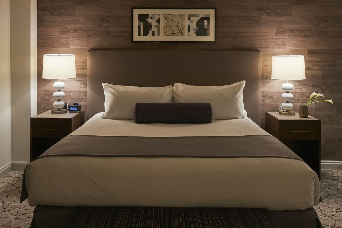 A neatly made bed with a headboard, two bedside tables with lamps, and a framed artwork above the headboard.