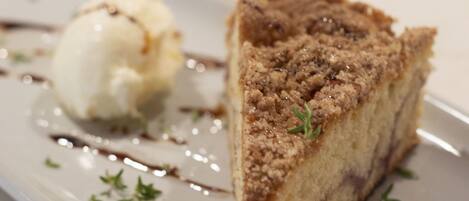 A slice of cake with a crumbly topping and a scoop of vanilla ice cream on a white plate.