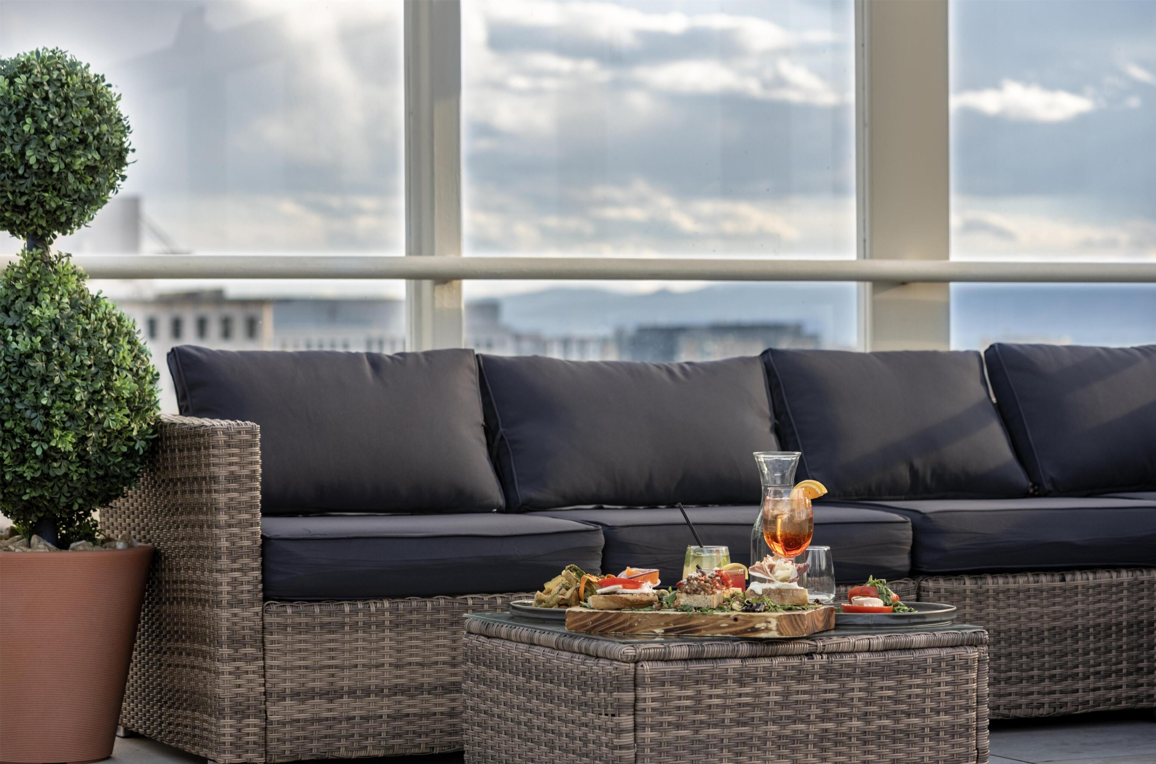 Een balkon met een rieten bank, een potplant en een tafel met eten en drinken.