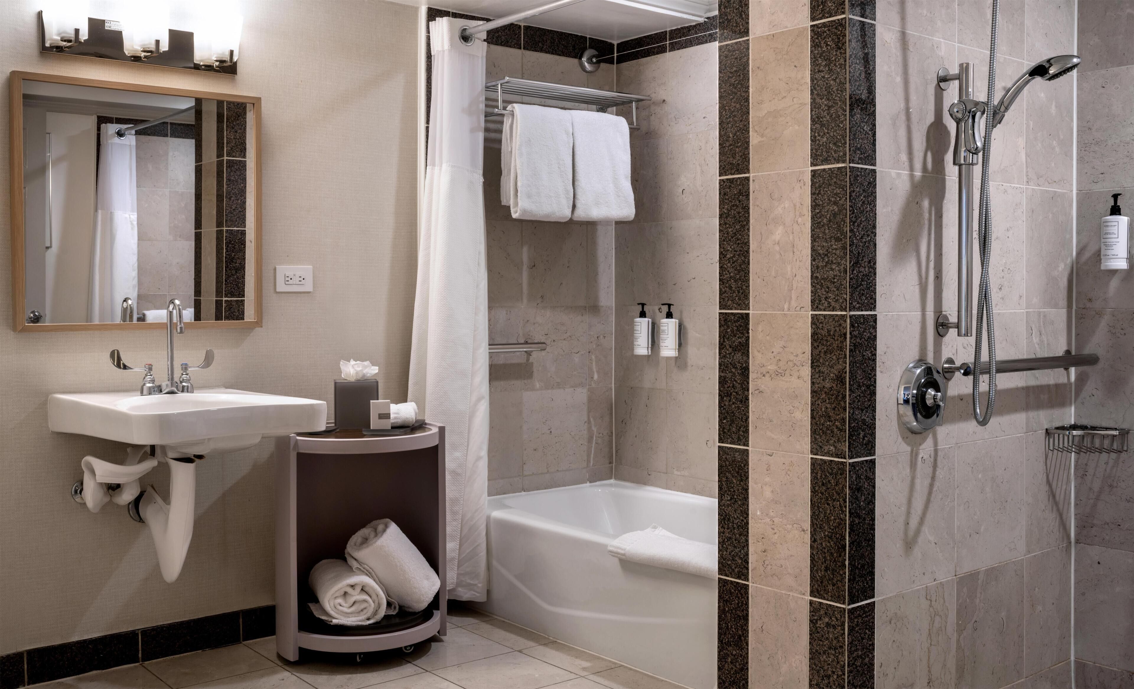 A hotel bathroom with a sink, mirror, towel rack, shower, and bathtub.