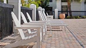A row of white lounge chairs aligned against a black metal fence on a paved walkway. - Orlando Palms Hotel (Orlando)