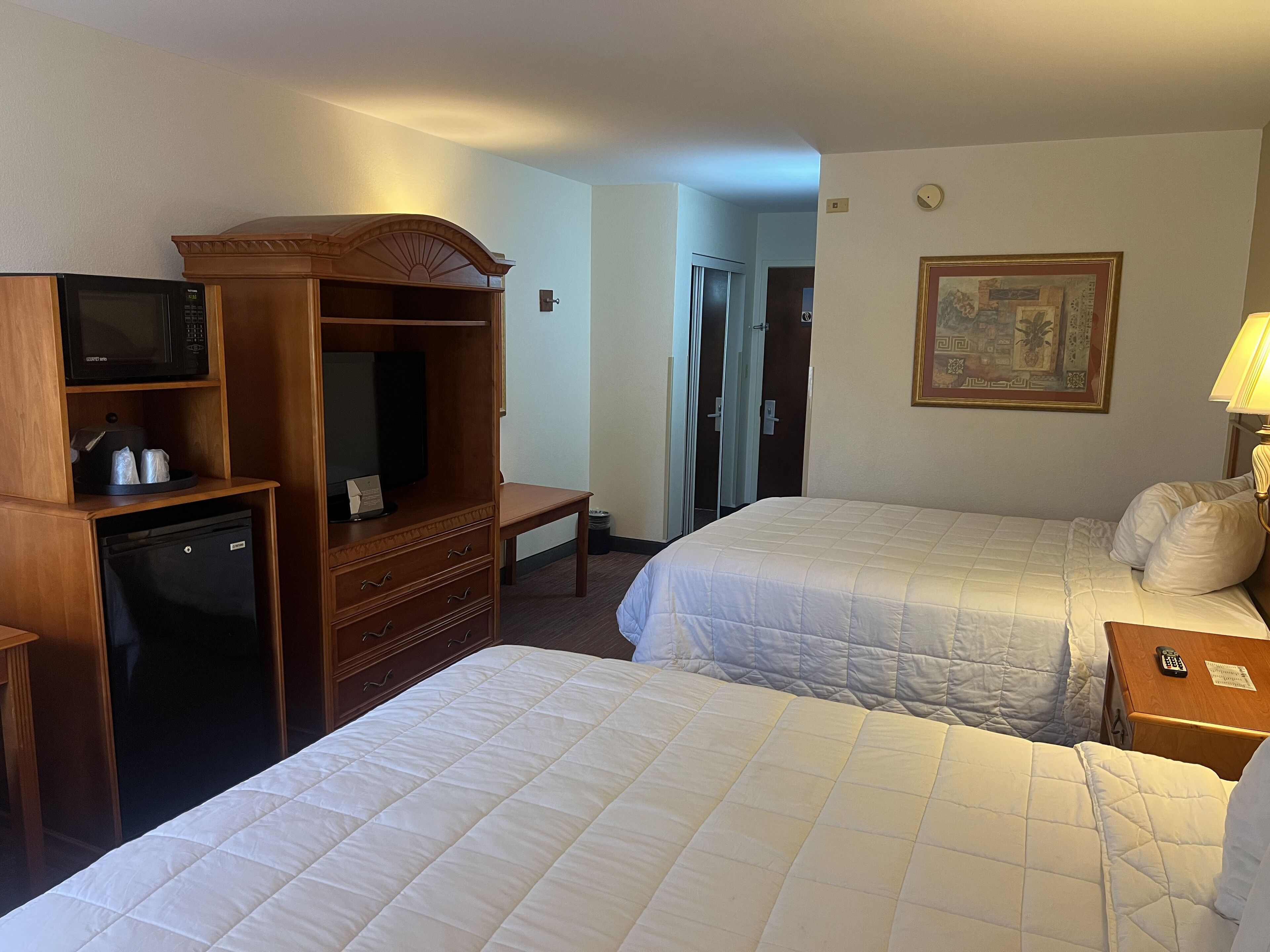 A hotel room with two beds, a TV, a minibar, and a desk.
