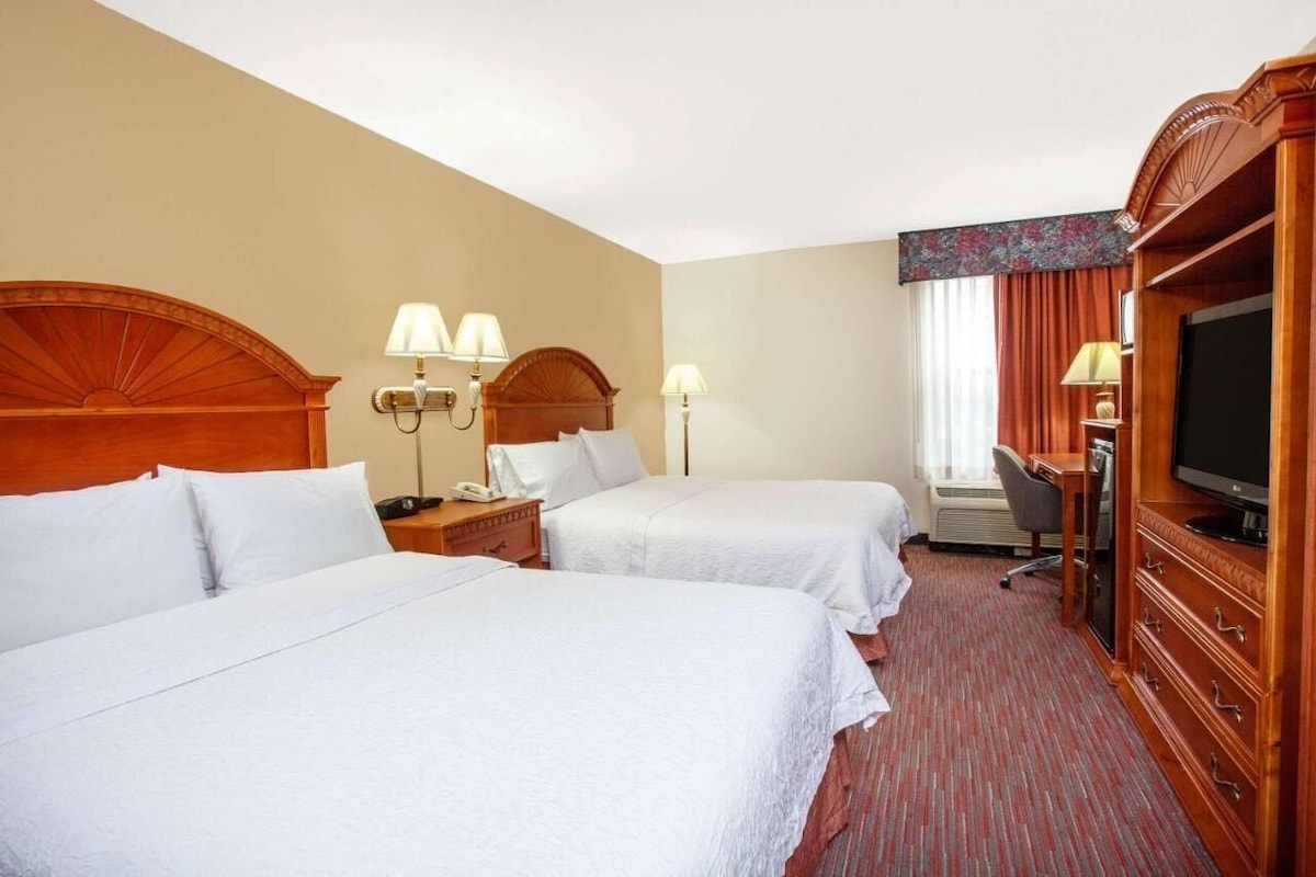 A hotel room with two beds, a television, a desk, and a chair.