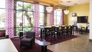 A hotel lobby with a dining area, large windows with curtains, a flat-screen TV, and a view of the outdoors. - Orlando Palms Hotel (Orlando)
