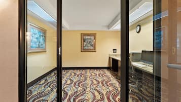 Une chambre d’hôtel avec un tapis à motifs, un bureau avec un ordinateur et un tableau accroché au mur.