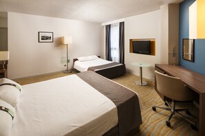 A hotel room with two beds, a desk, a chair, a TV, and a picture on the wall.