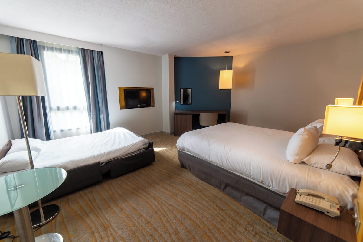 A hotel room with two beds, a desk, a chair, a lamp, and a phone on the nightstand.