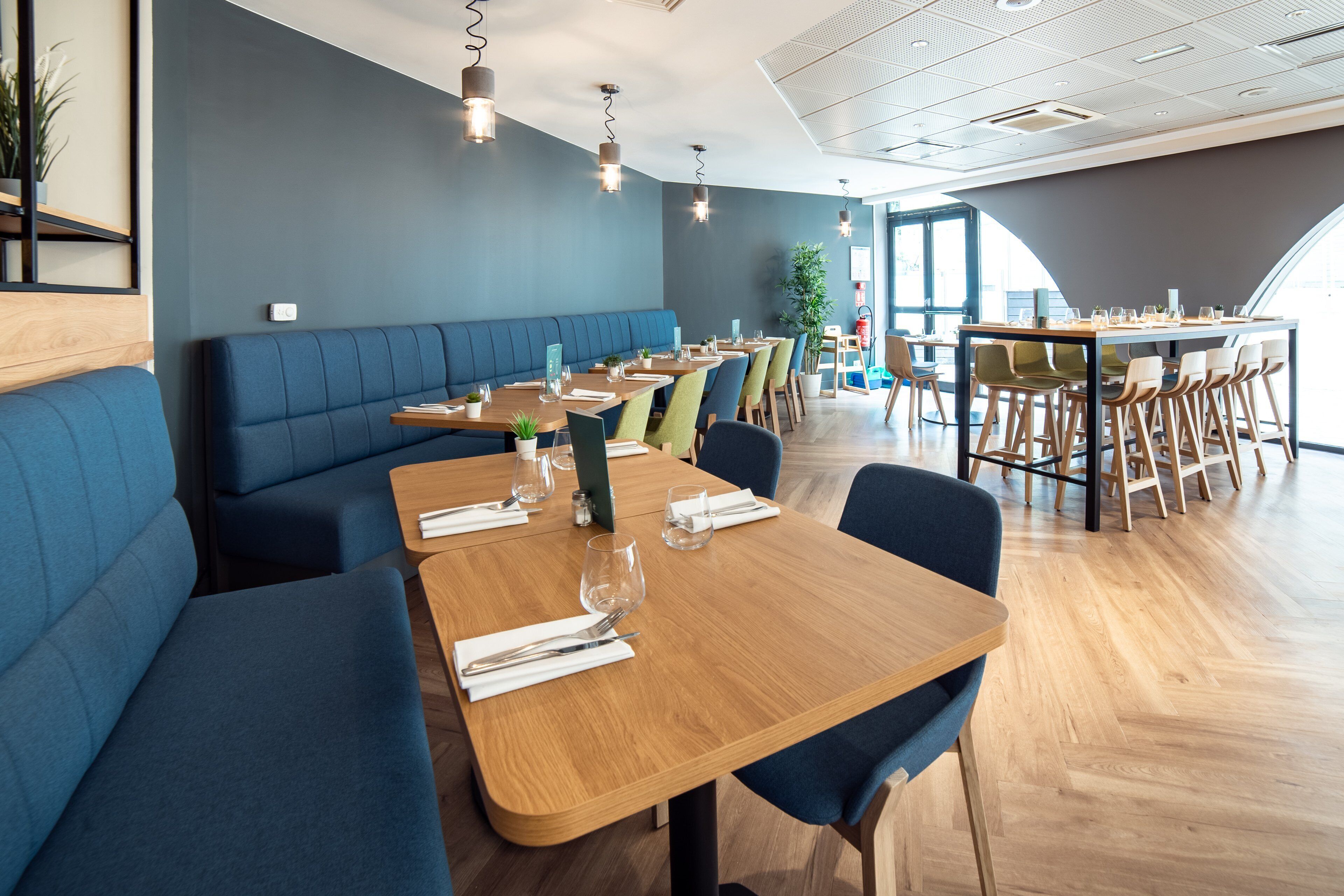 Un restaurant moderne avec des sièges bleus, des tables en bois et des luminaires suspendus.