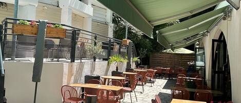 An outdoor cafe with tables and chairs, covered by a green canopy, and potted plants on the walls.