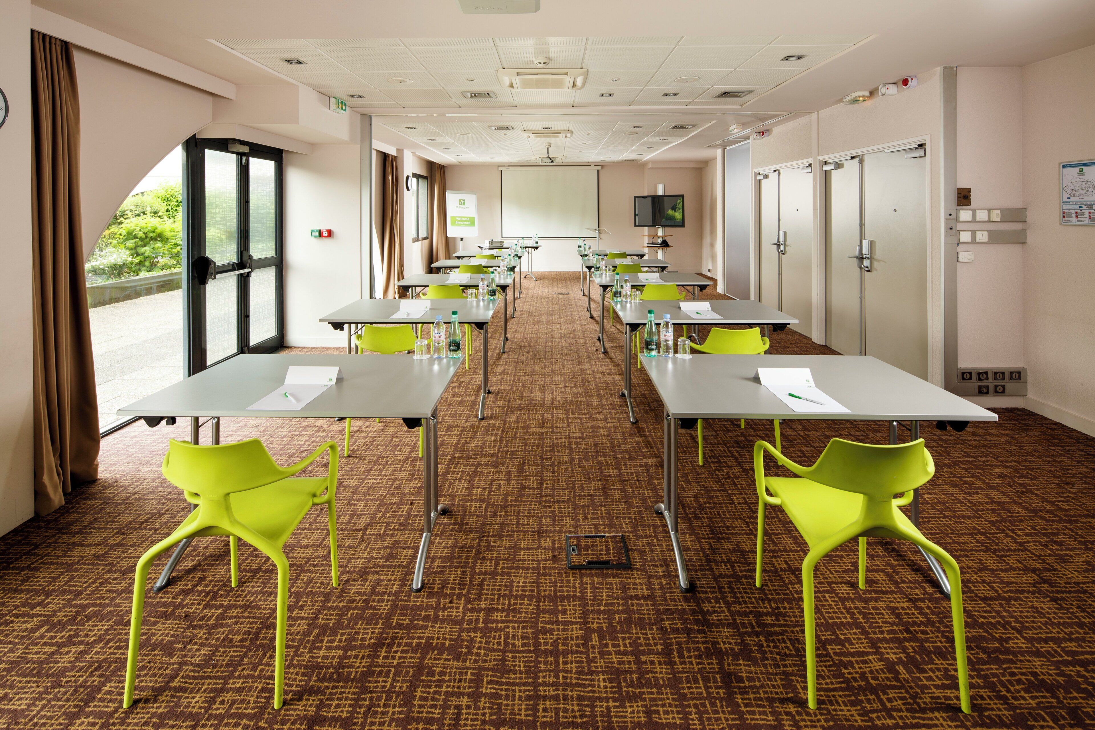 A conference room with tables, chairs, a projector screen, and a large window.