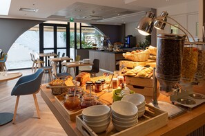 Ein Frühstücksbuffet mit verschiedenen Speisen, einer Kaffeestation und Sitzgelegenheiten.