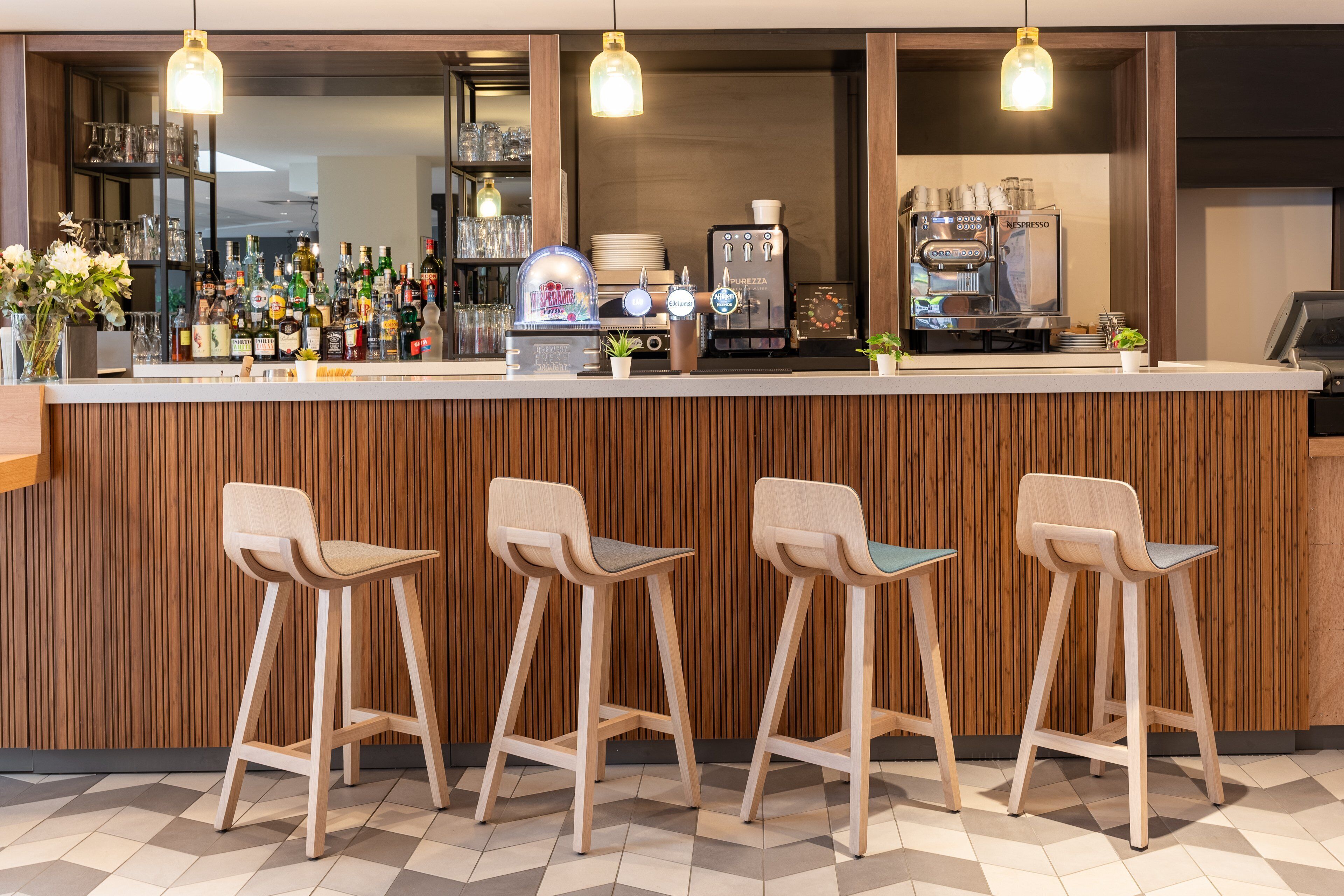 A bar area with a wooden counter, bar stools, and a coffee machine.
