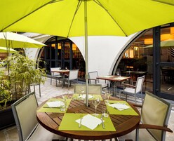 Un área de comedor al aire libre con mesas, sillas y sombrillas.