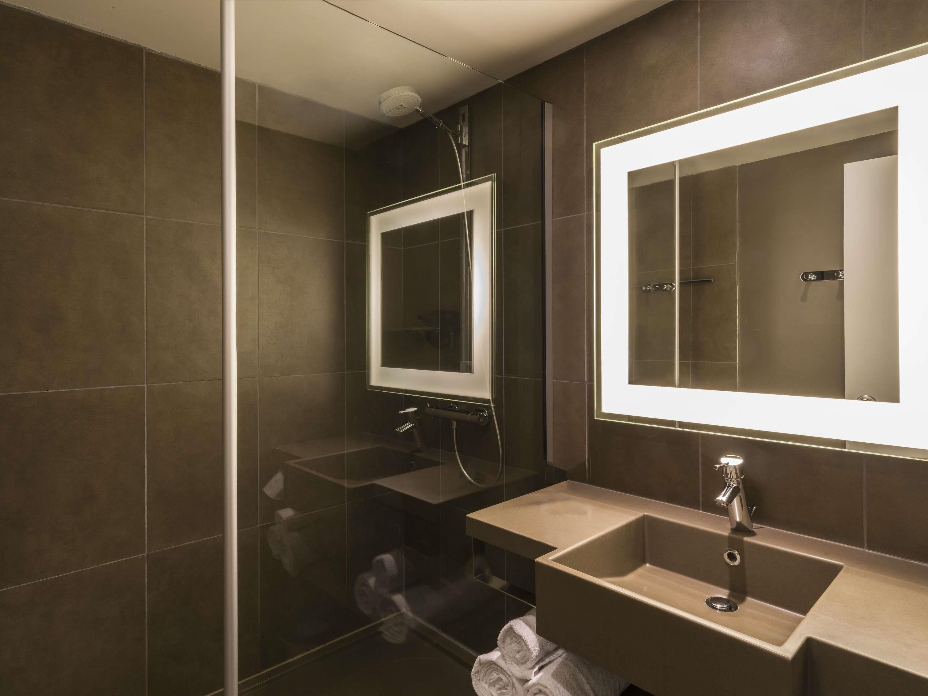 A modern bathroom with a glass shower enclosure, a large mirror, and a sink with a faucet.