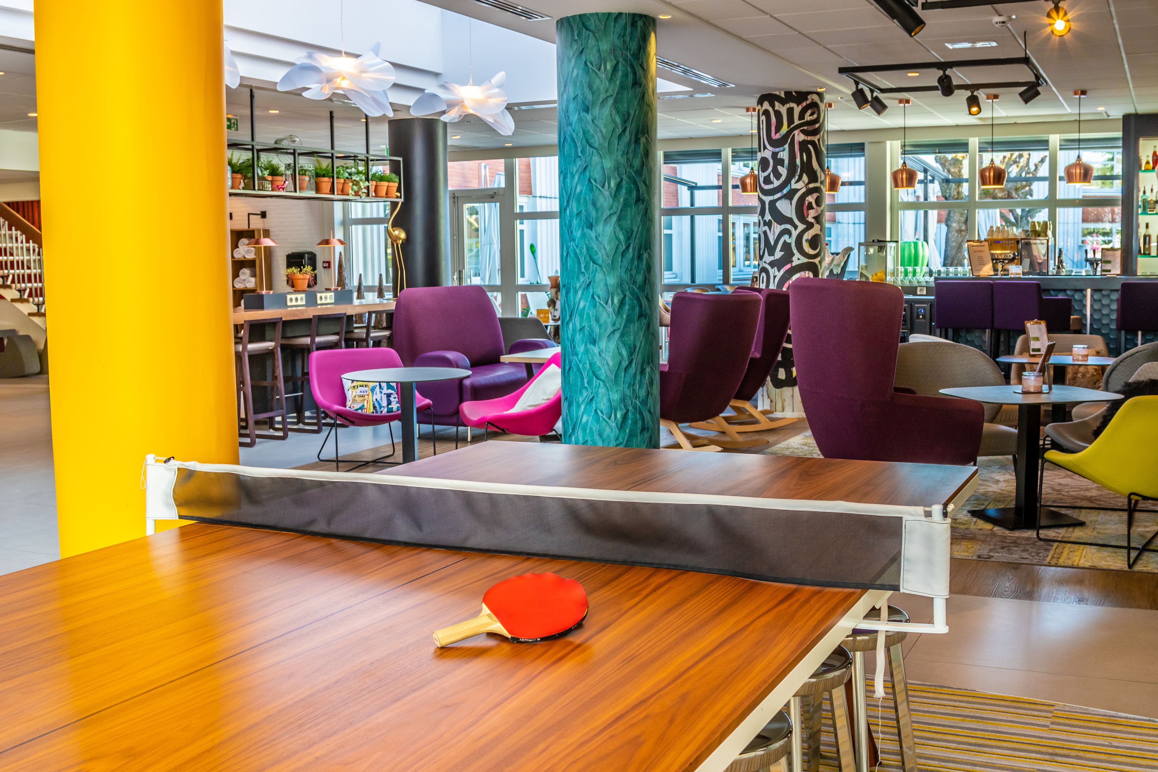 A modern indoor space with a ping pong table, purple and yellow chairs, and a large teal pillar.