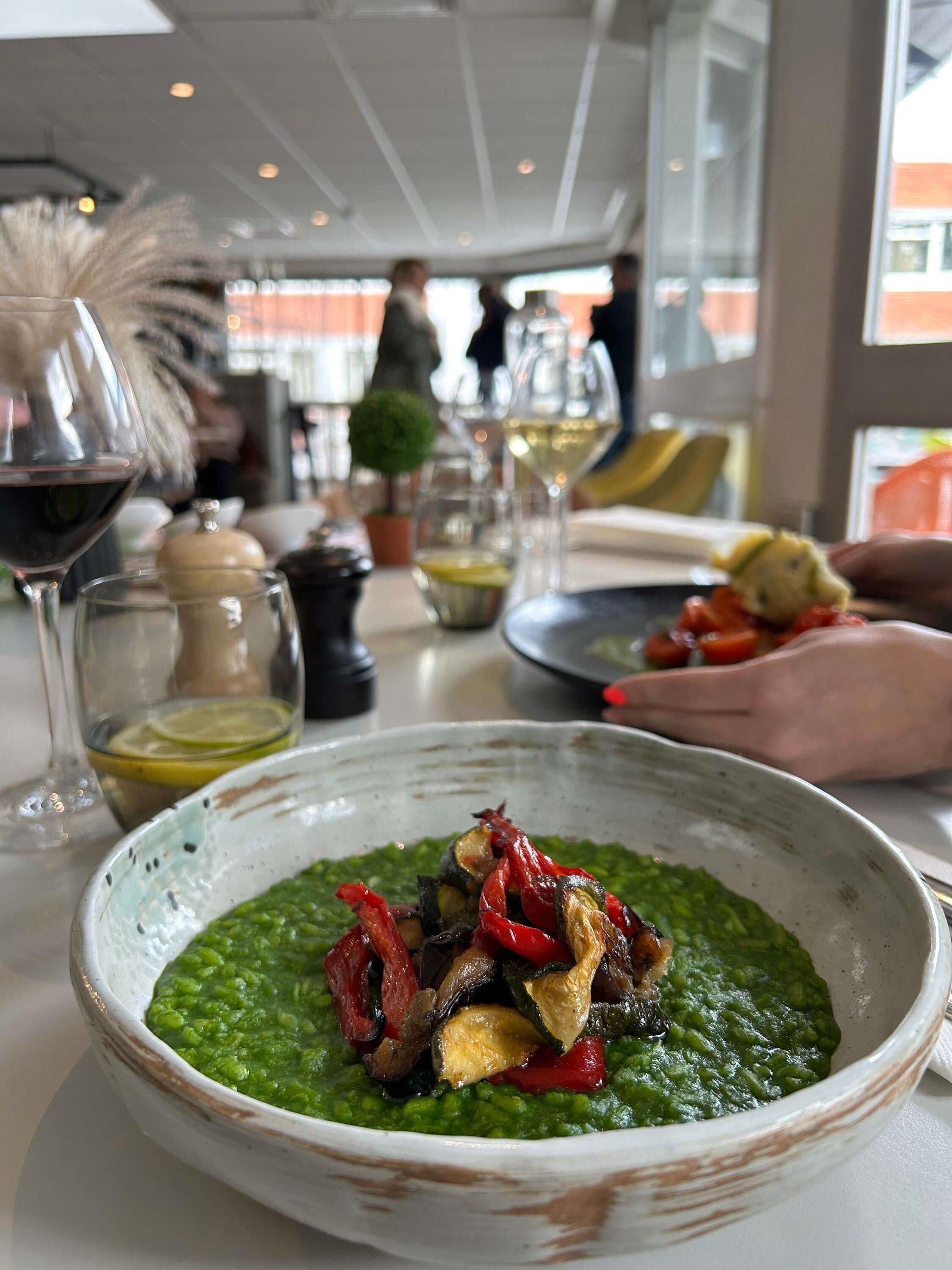 Una mesa de comedor con un bol de salsa verde y verduras, copas de vino y un salero y pimentero.