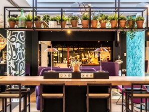 A restaurant with a bar area, purple seating, and potted plants on the bar counter. - Novotel Lyon Bron Eurexpo (Bron)