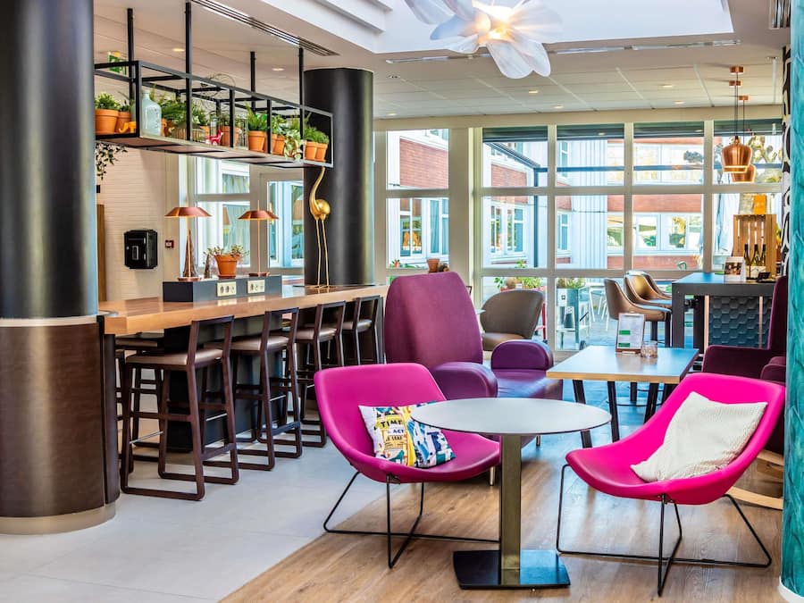 Un intérieur moderne avec un espace bar, des sièges confortables dotés de chaises aux couleurs vives et de grandes fenêtres offrant une vue sur l’extérieur.