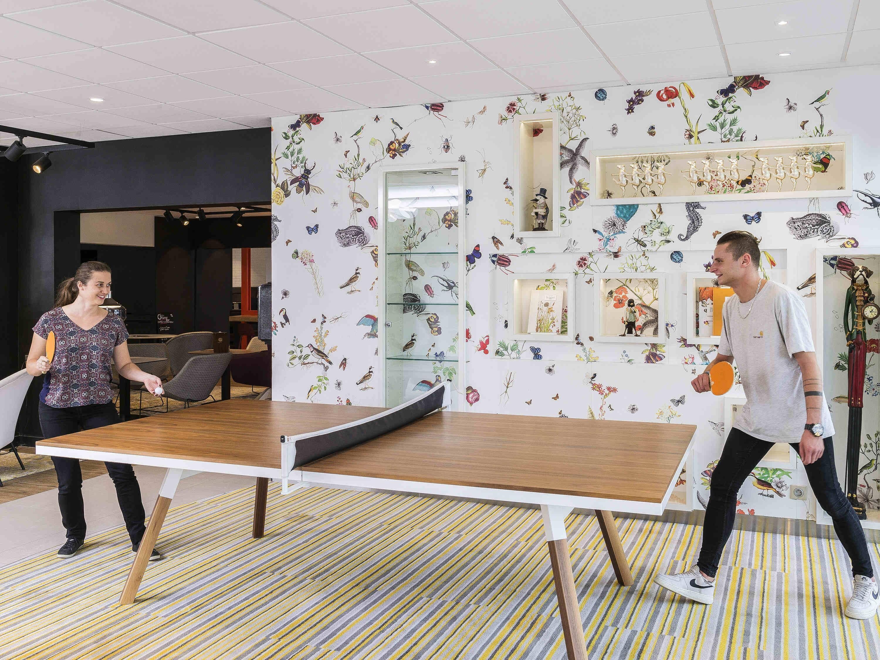 A ping pong table in a room with a floral wall mural and a striped carpet.