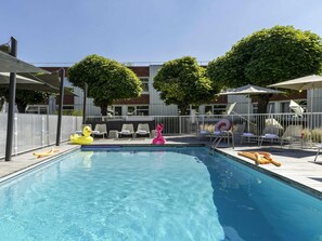 A swimming pool with lounge chairs and umbrellas, surrounded by a fence and trees. - Novotel Lyon Bron Eurexpo (Bron)